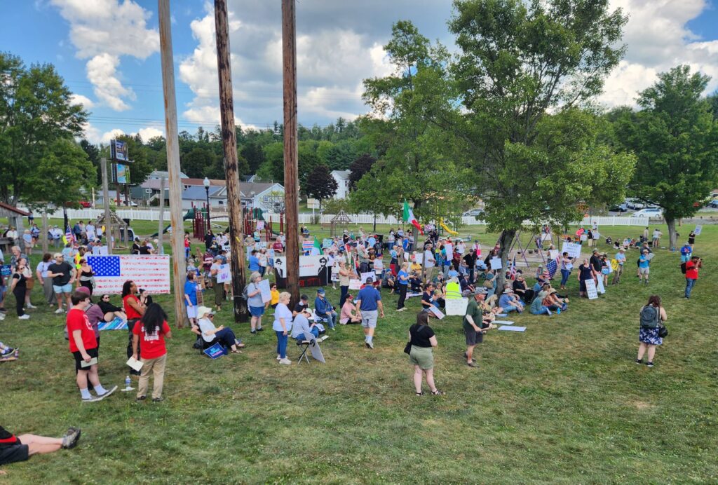 Protesters holding signs on a grassy area with multiple trees.